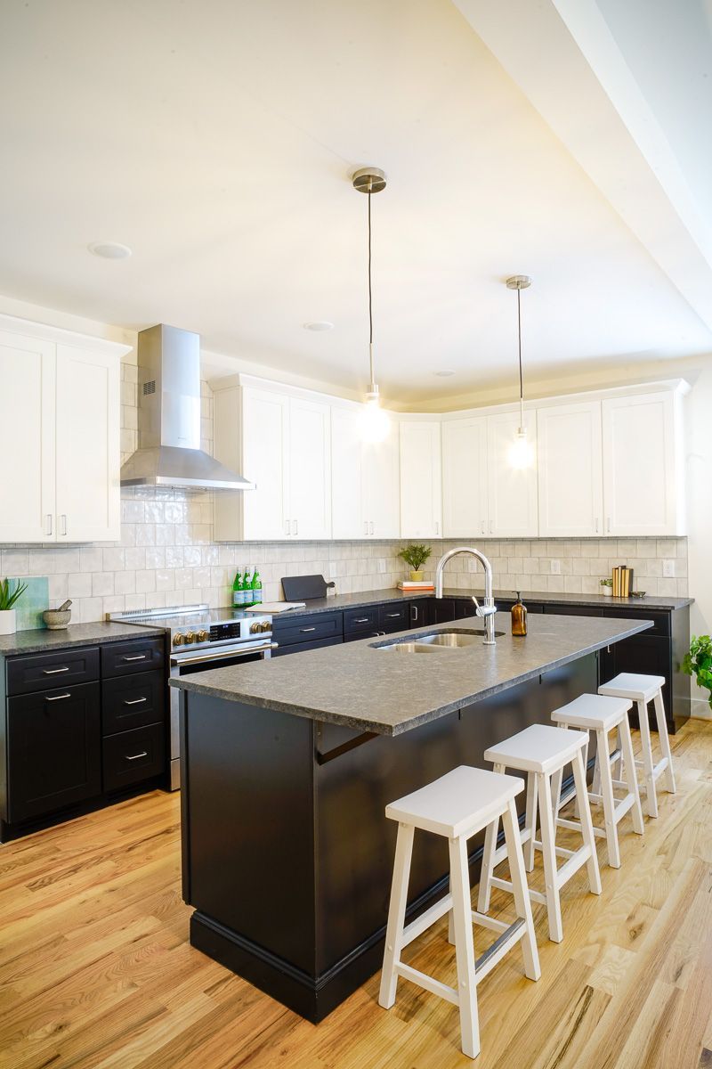 Bright modern kitchen with black island, white cabinets, and stools on wood floor