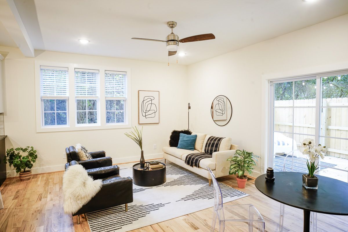Bright modern living room with white walls, black chairs, sofa, rug, and large windows.