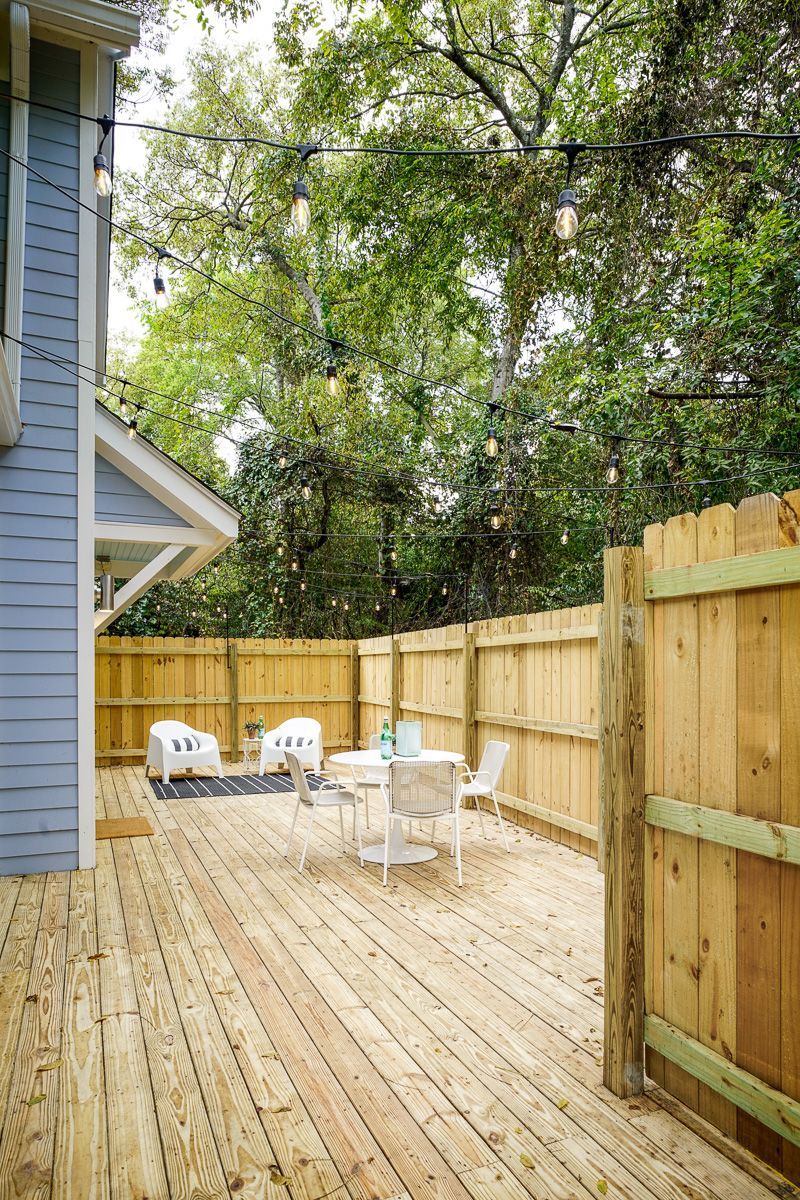 Wooden backyard deck with fence, patio chairs, and trees beside a blue house