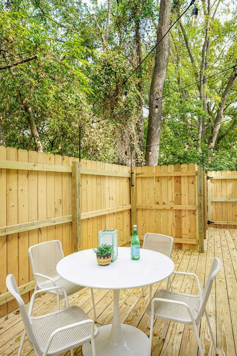 Small backyard patio with white table and chairs beside a wooden fence and trees