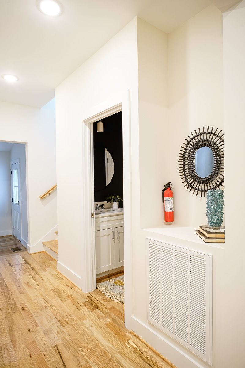 Bright hallway with wood floors, a doorway, wall decor, and a fire extinguisher on a white wall.