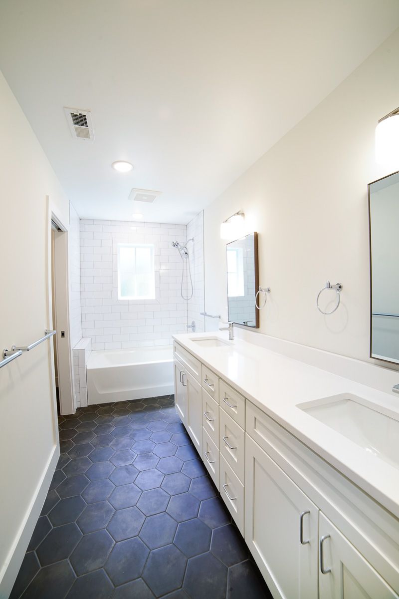 Bright white bathroom with double vanity, mirrors, hex tile floor, and a tub/shower at the far end.