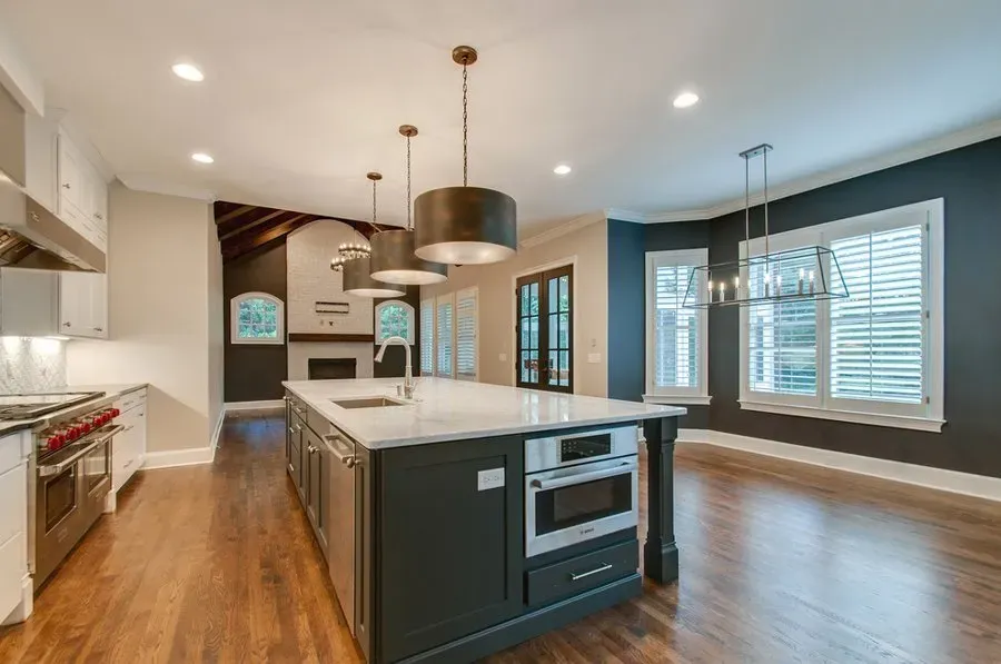Modern kitchen with island, hardwood floors, white cabinets, and large windows in an open living space