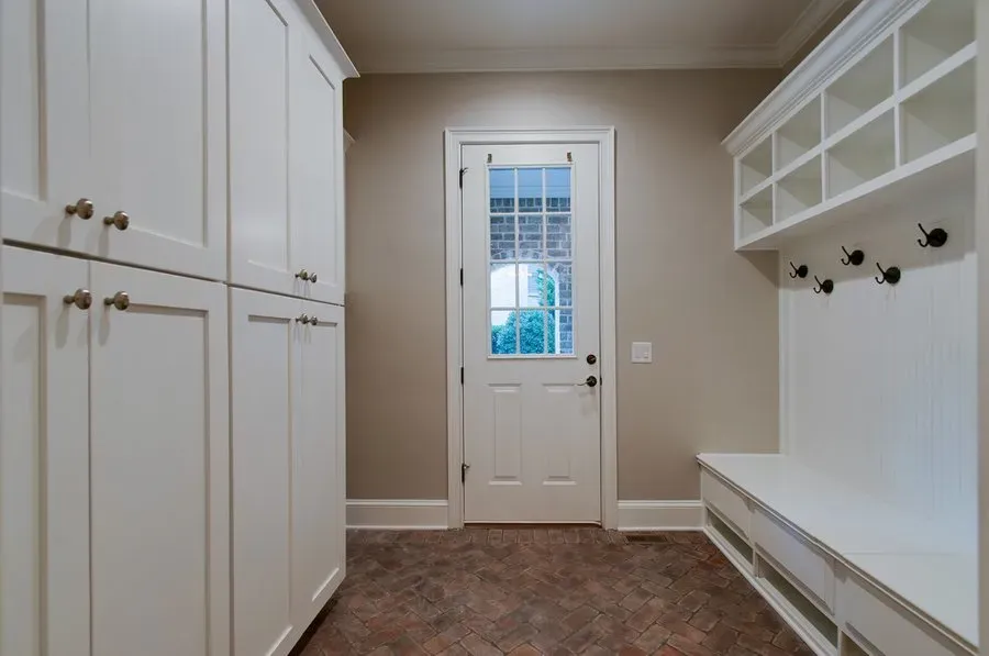 Bright mudroom with white cabinets, bench, coat hooks, and a glass-paneled door.