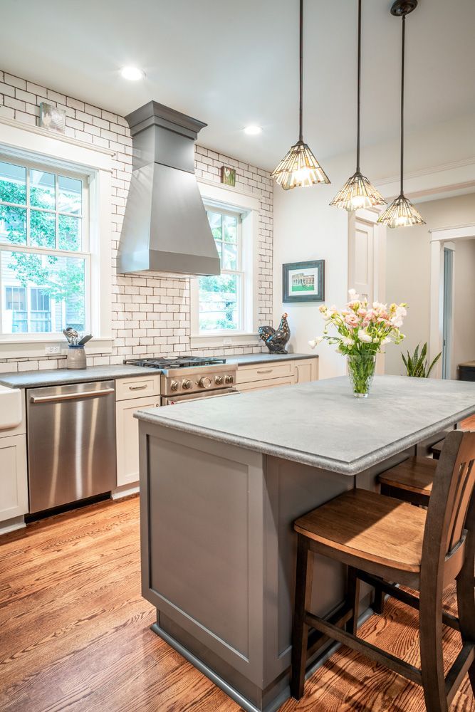 Bright kitchen with gray island, white brick backsplash, stainless appliances, and pendant lights