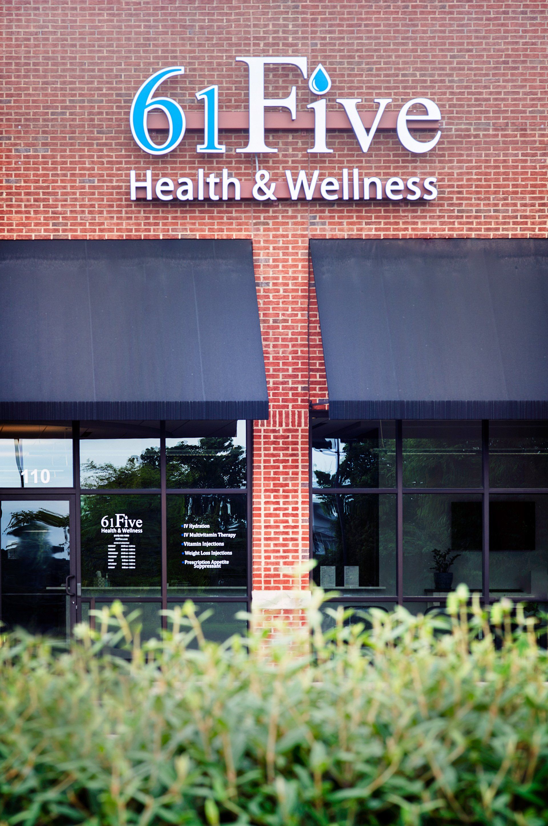 Storefront sign for “61Five Health & Wellness” on a brick building with dark awnings and shrubs in front