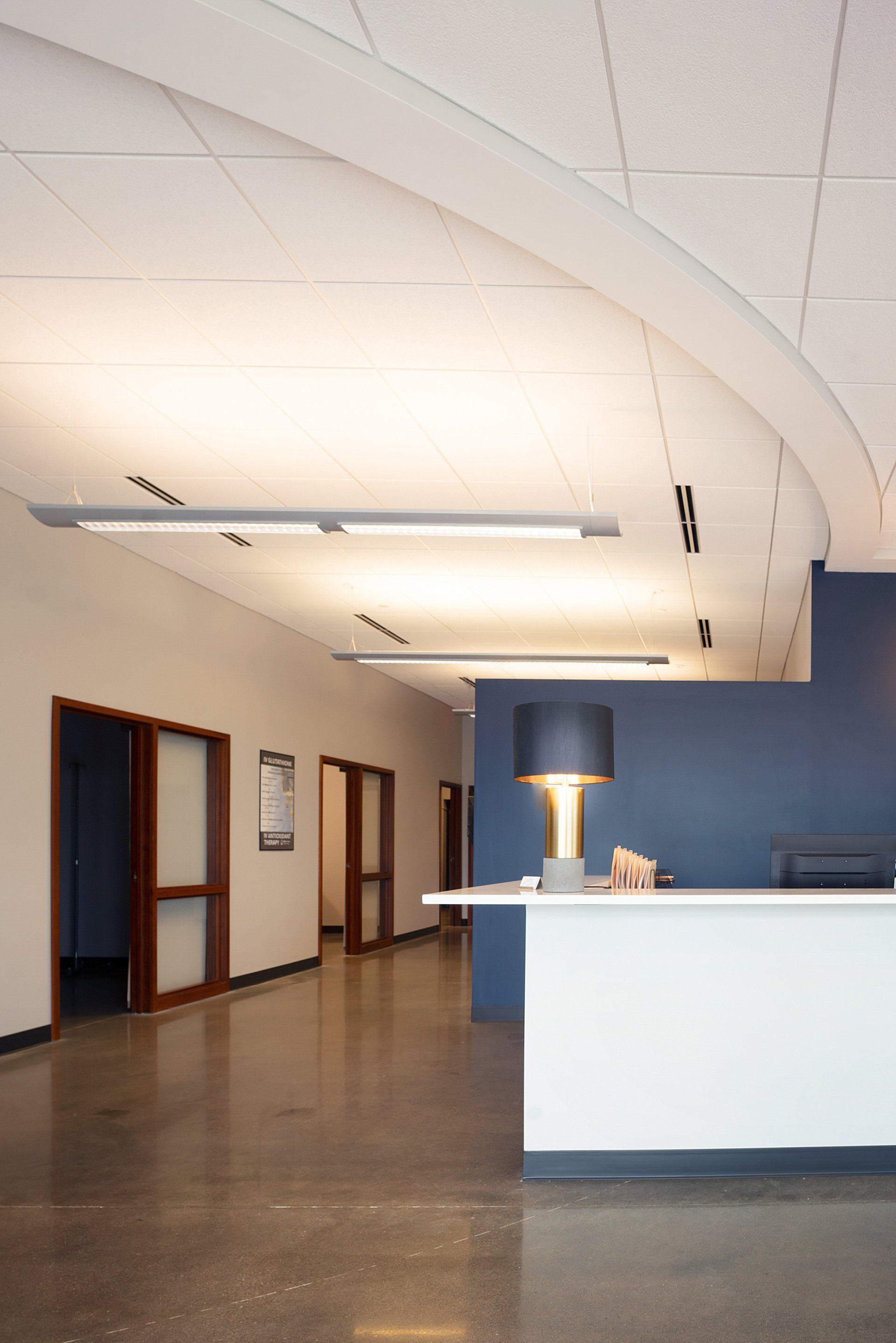 Quiet office lobby with white ceiling, blue wall, reception desk, and hallway doors on the left.