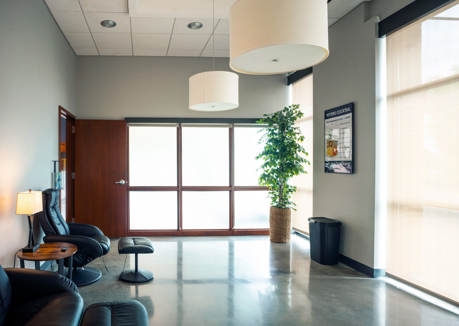 Empty modern lobby with lounge chairs, pendant lights, a potted plant, and large windows.
