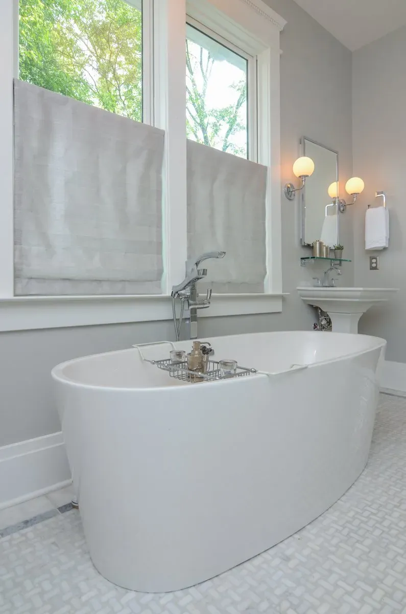 Bright bathroom with a white freestanding tub, tiled floor, windows, and wall sconces