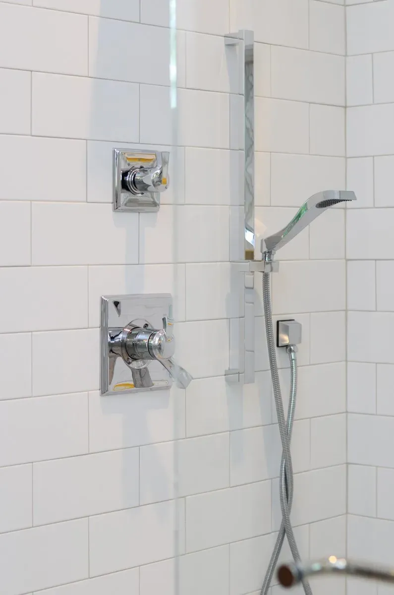 Walk-in shower with white tile, chrome fixtures, handheld showerhead, and grab bar