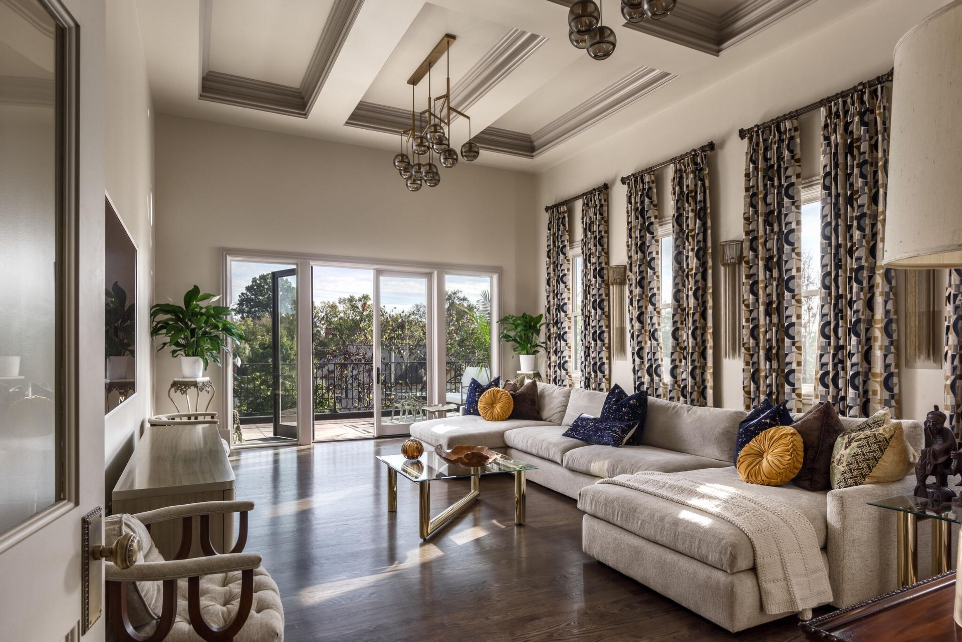 Bright living room with a cream sectional, patterned curtains, and open doors to a sunny patio.
