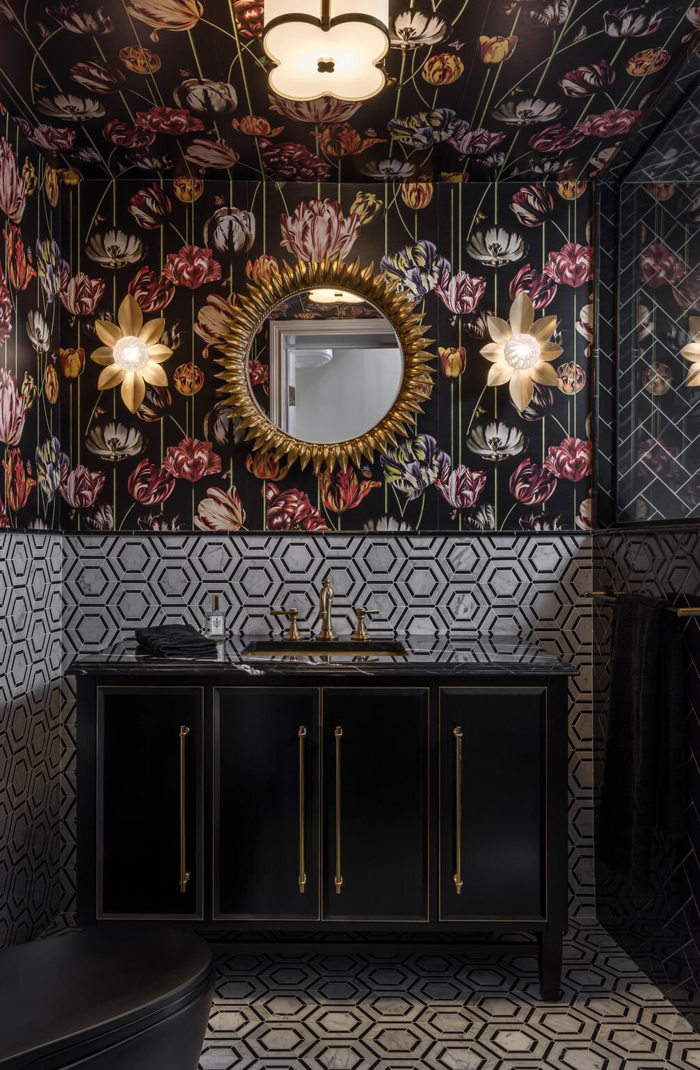 Black vanity with gold accents in a floral wallpapered bathroom, framed mirror, and hanging star lights