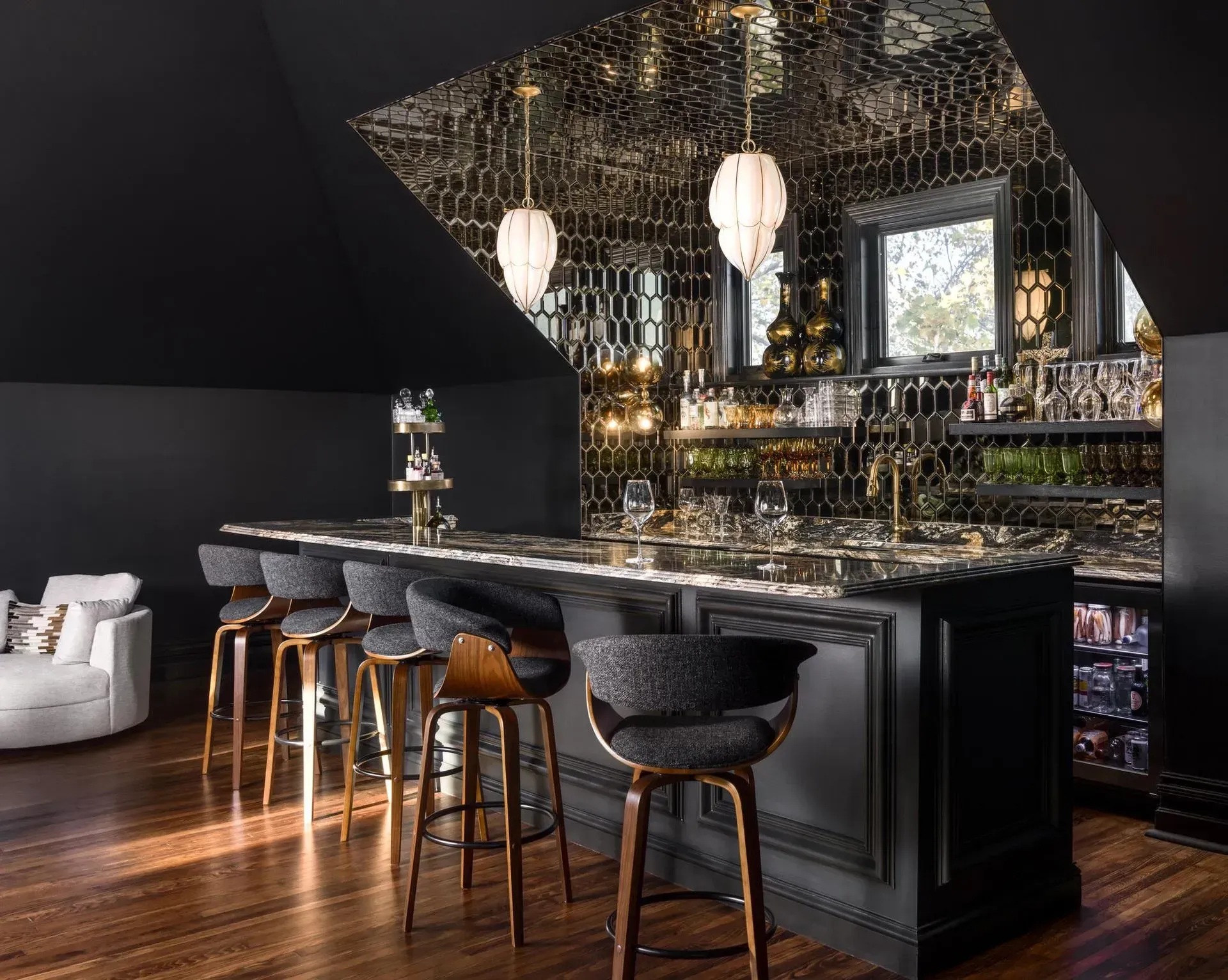 Luxurious black-and-gold home bar with stools, mirrored backsplash, pendant lights, and hardwood floors