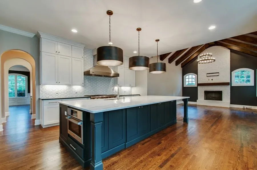 Modern kitchen with navy island, white cabinets, wood floors, and open living area with fireplace