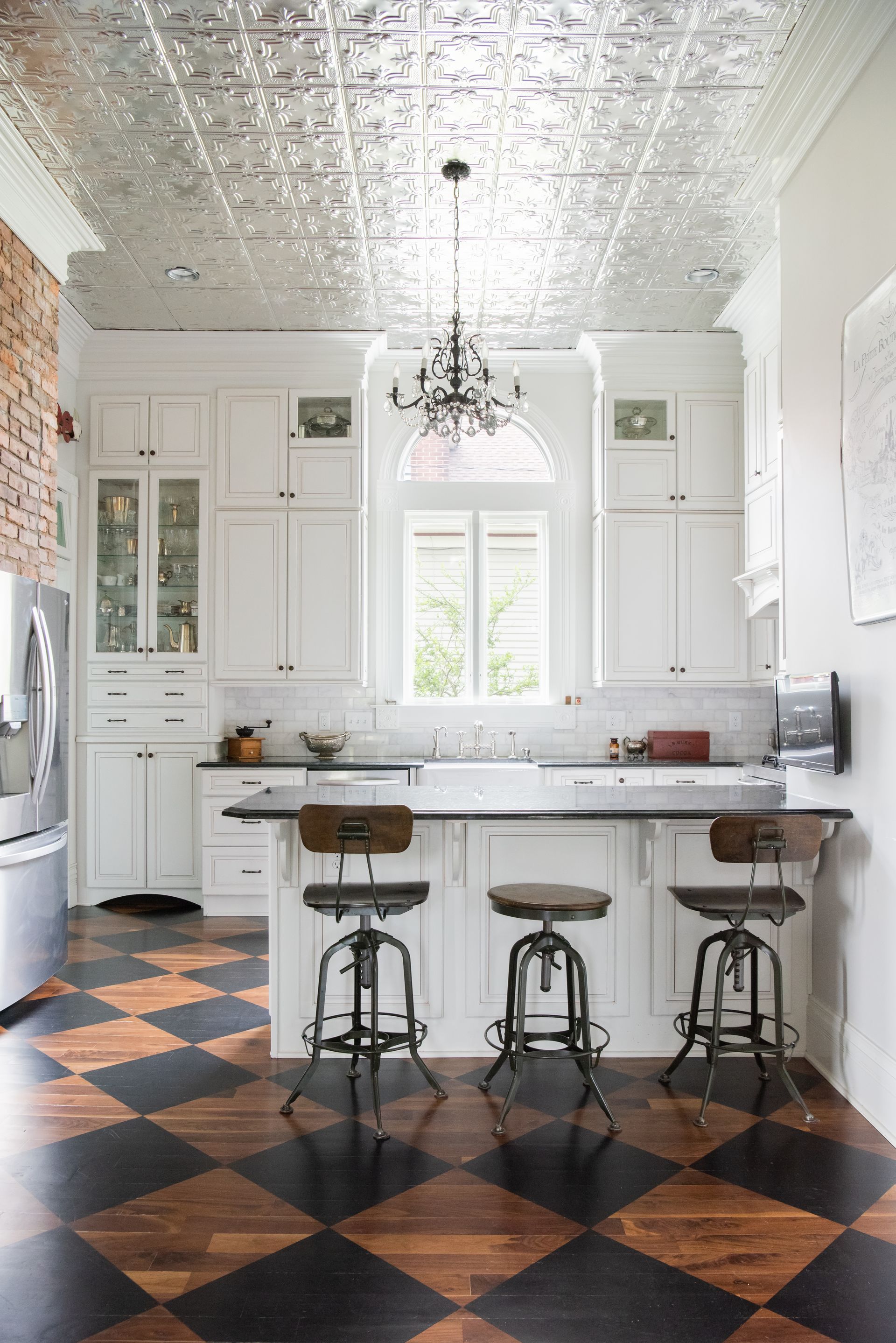 Bright white kitchen with bar stools, chandelier, and black-and-copper checkered floor.