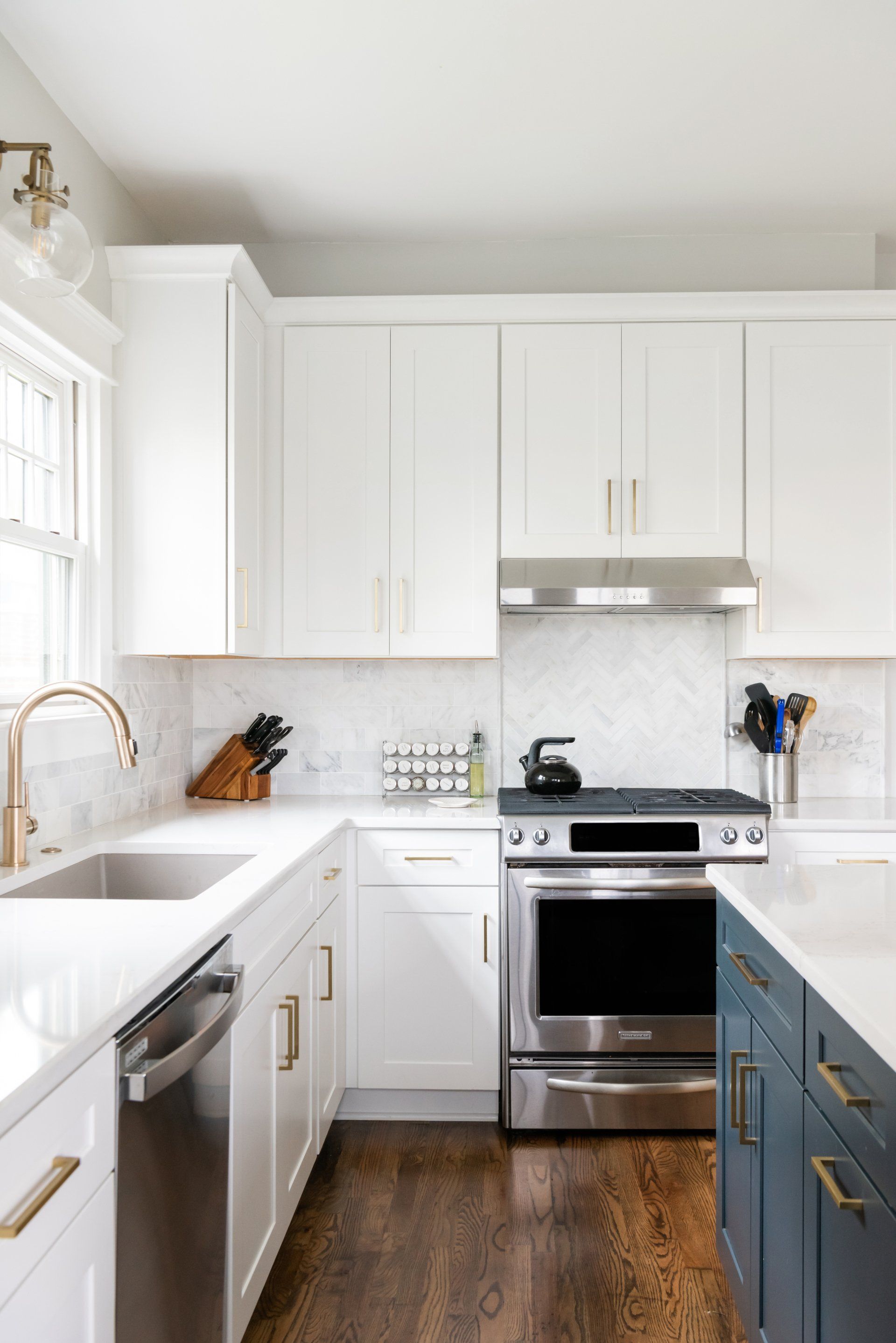 Bright white kitchen with stainless steel stove, dark wood floor, and blue lower cabinets