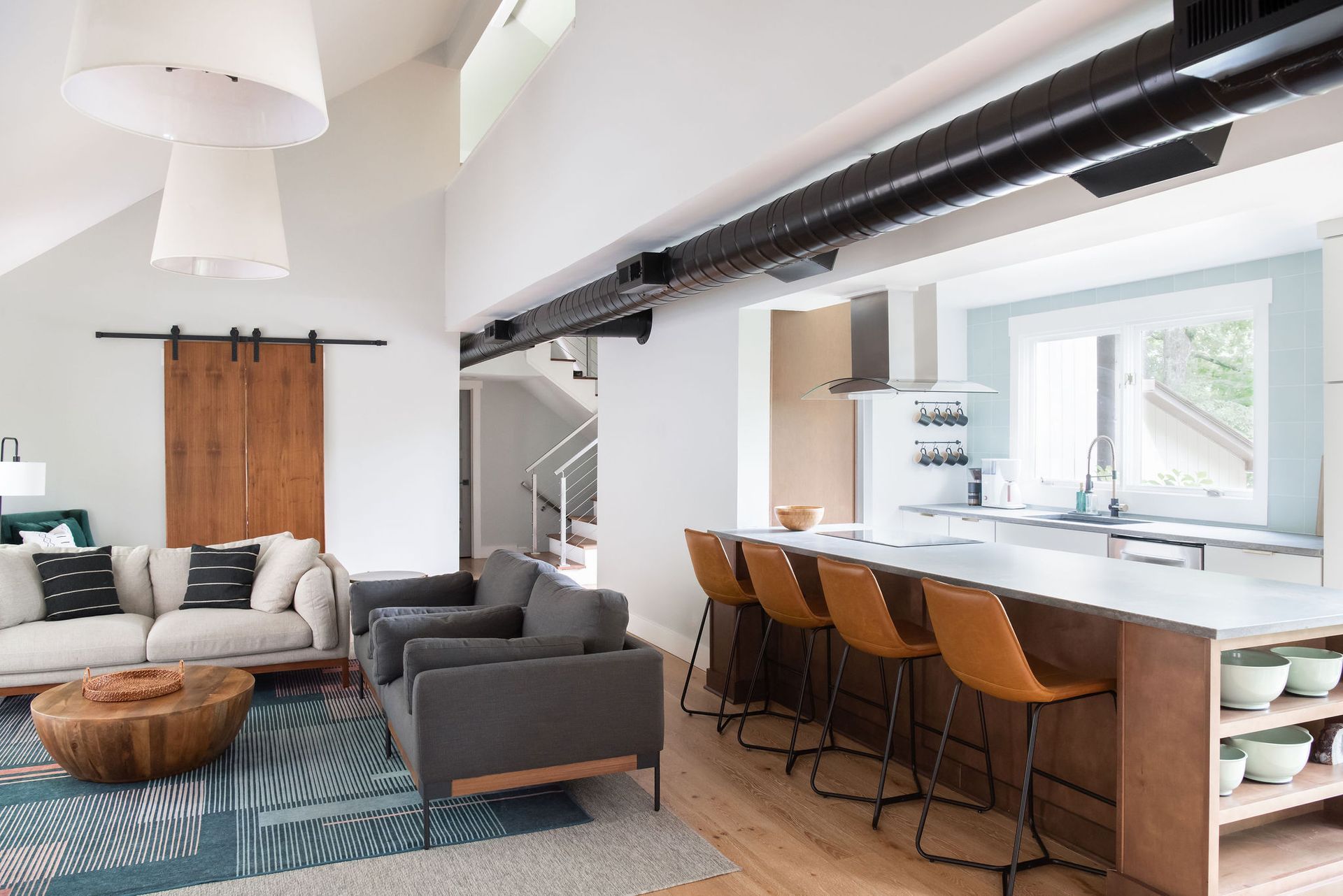 Bright open-plan living room with gray sofas, woven coffee table, and a kitchen island with bar stools