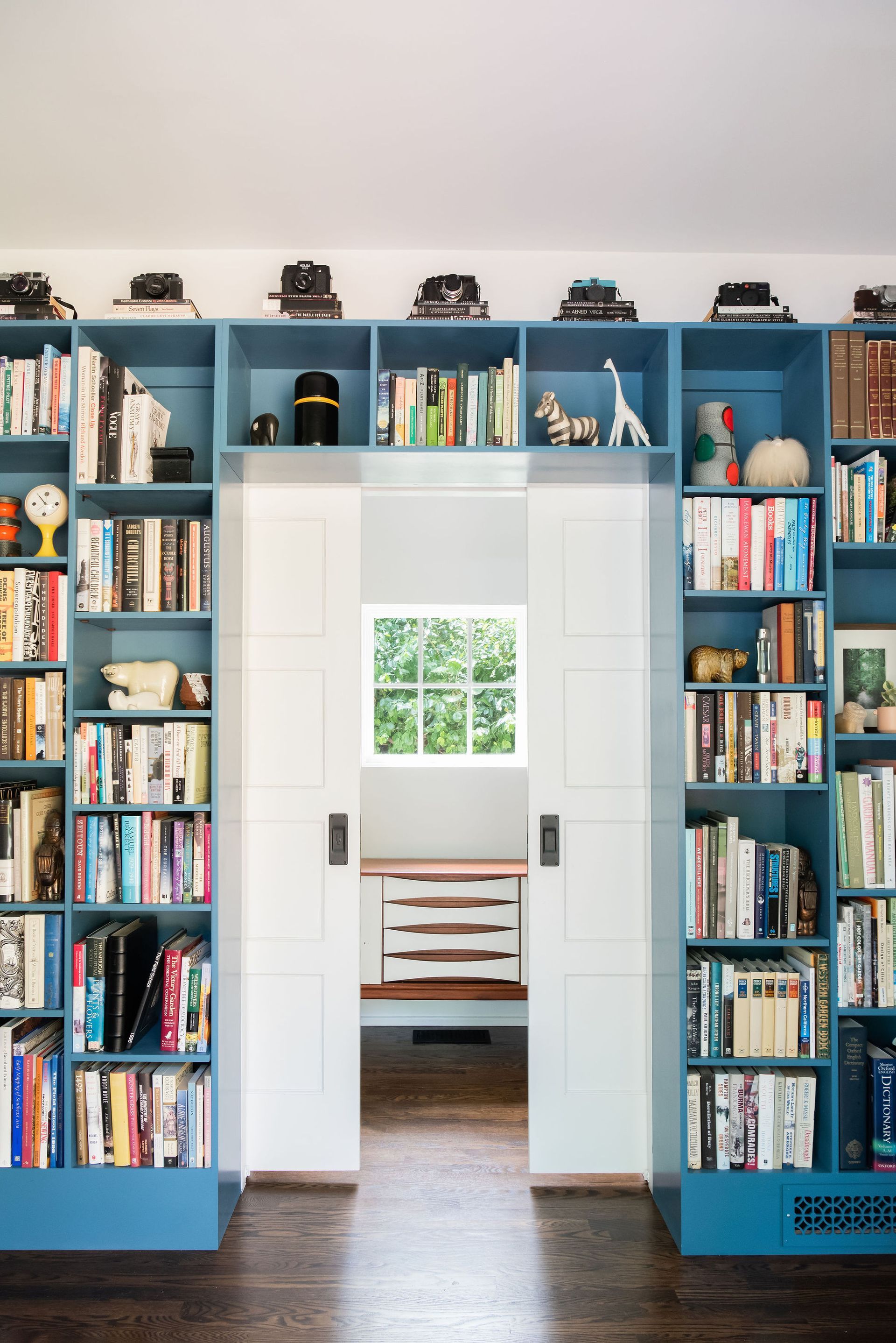 Open white doorway framed by blue bookshelves, leading to a bright room with a window and bench.