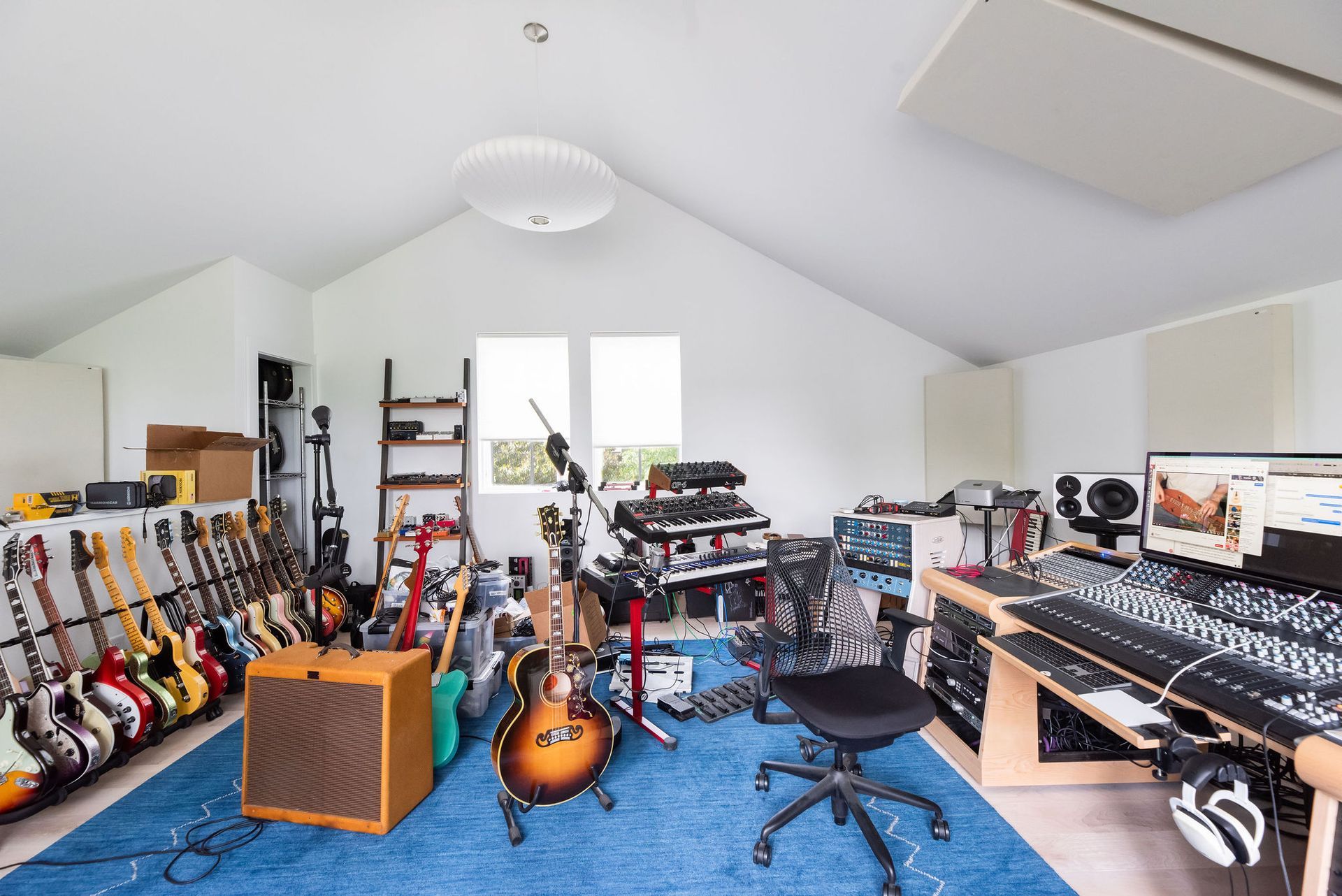 Home music studio with guitars, keyboard, drum set, recording gear, and blue carpet.