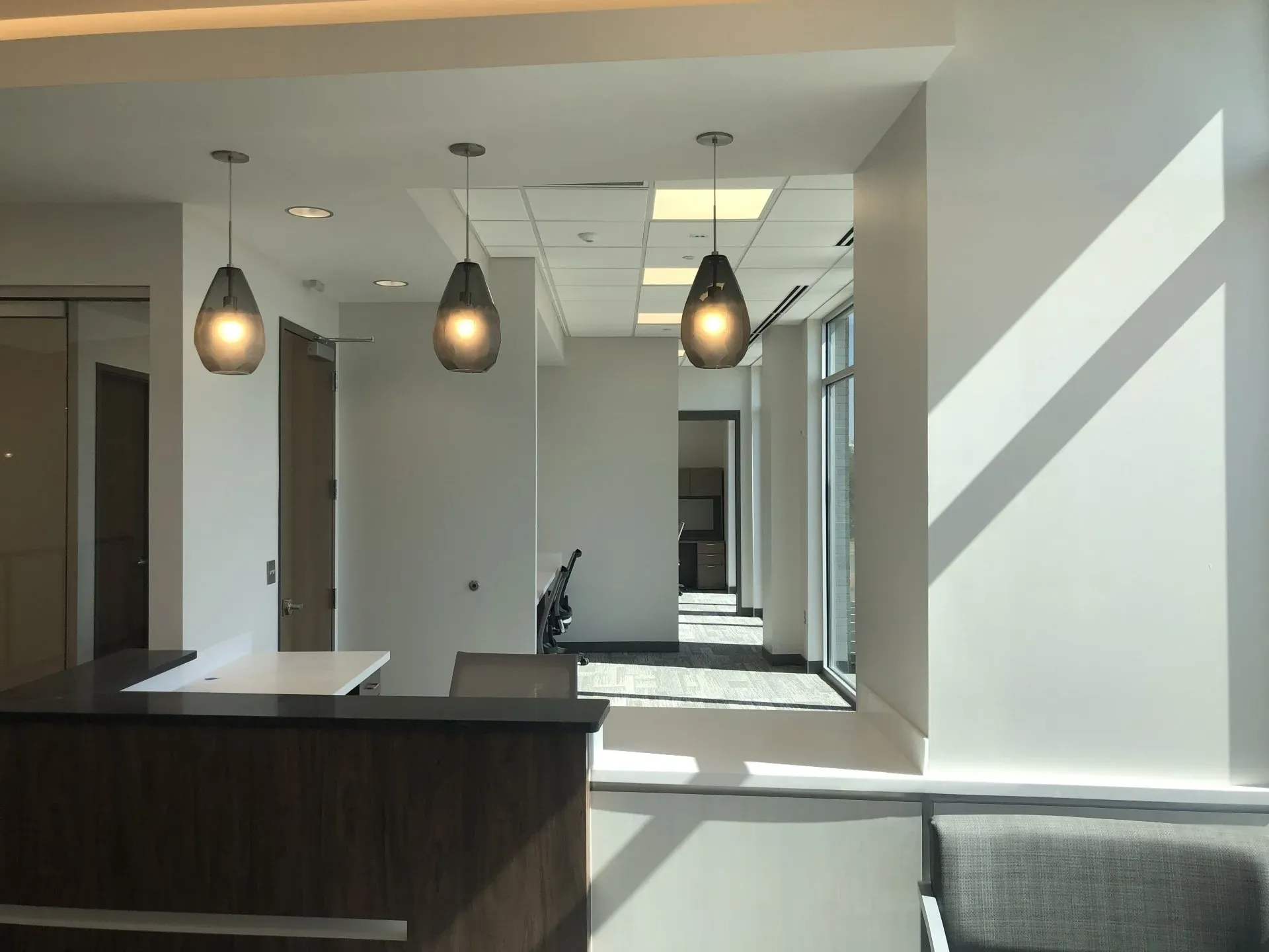 Modern minimalist kitchen with dark island, pendant lights, and sunlight casting shadows on white walls.