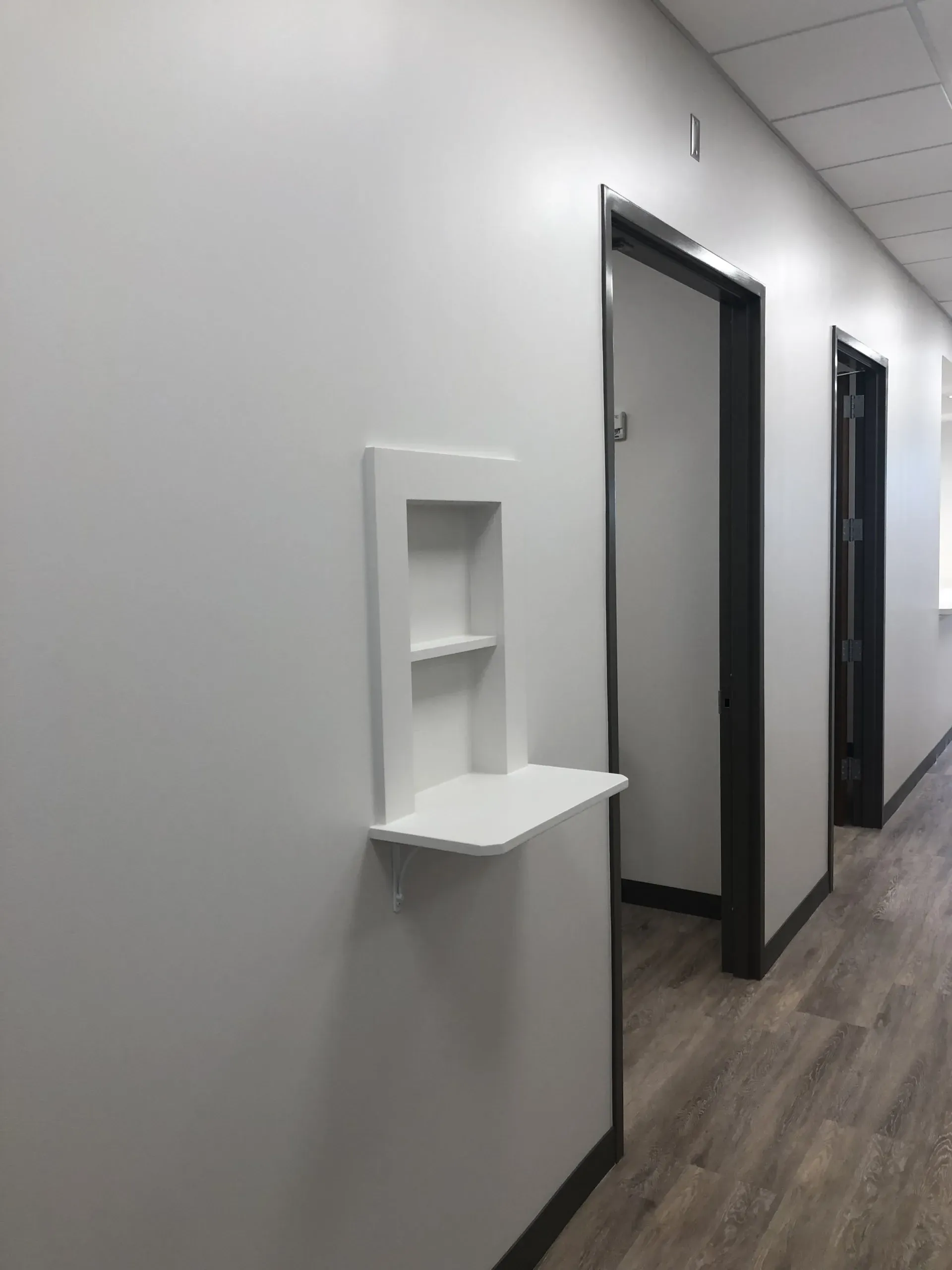Empty hallway with white walls, wood-look floor, and a small wall-mounted shelf near open doorways