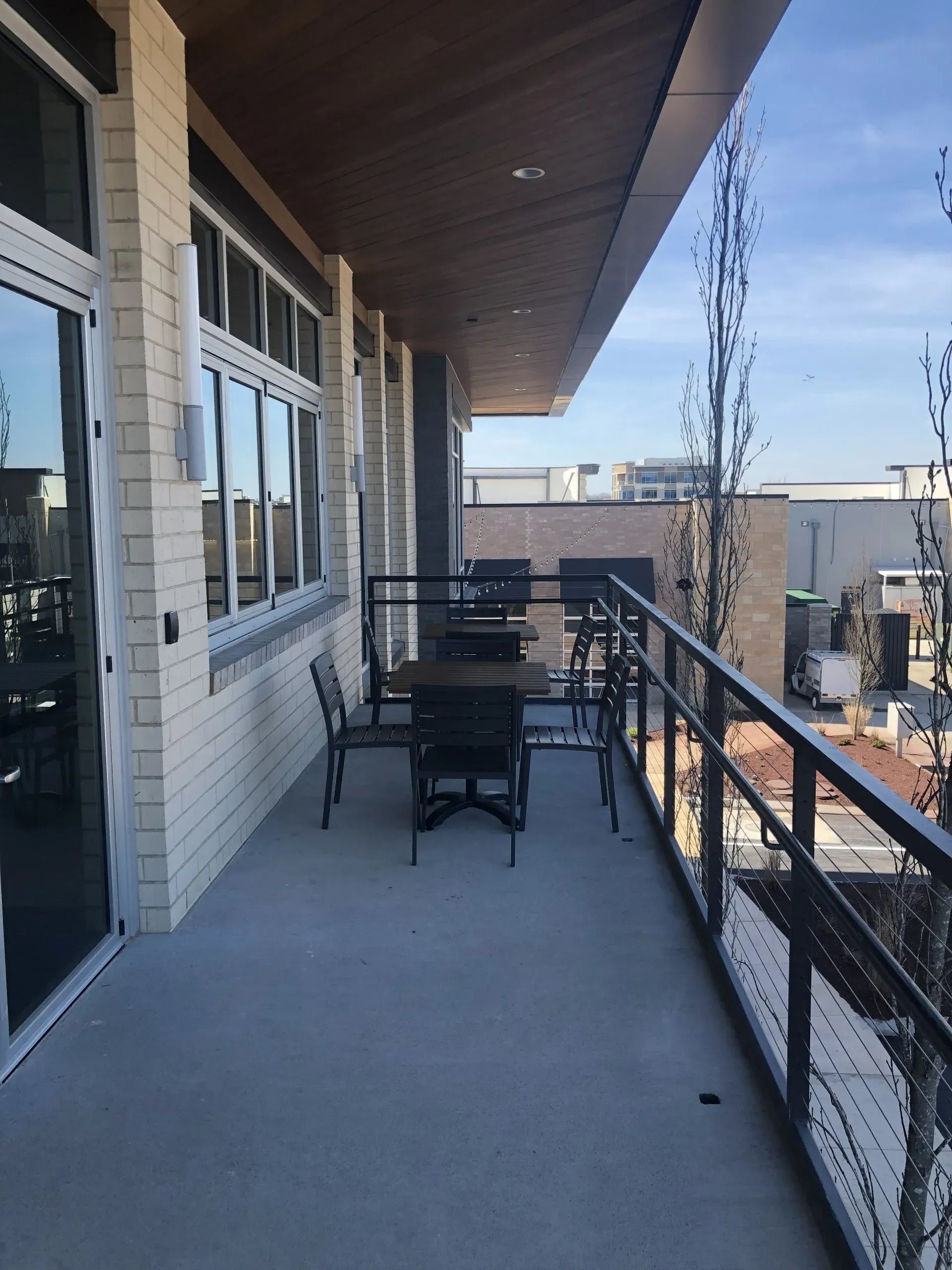 Apartment balcony with black railing, patio chairs, and a table overlooking an outdoor view.