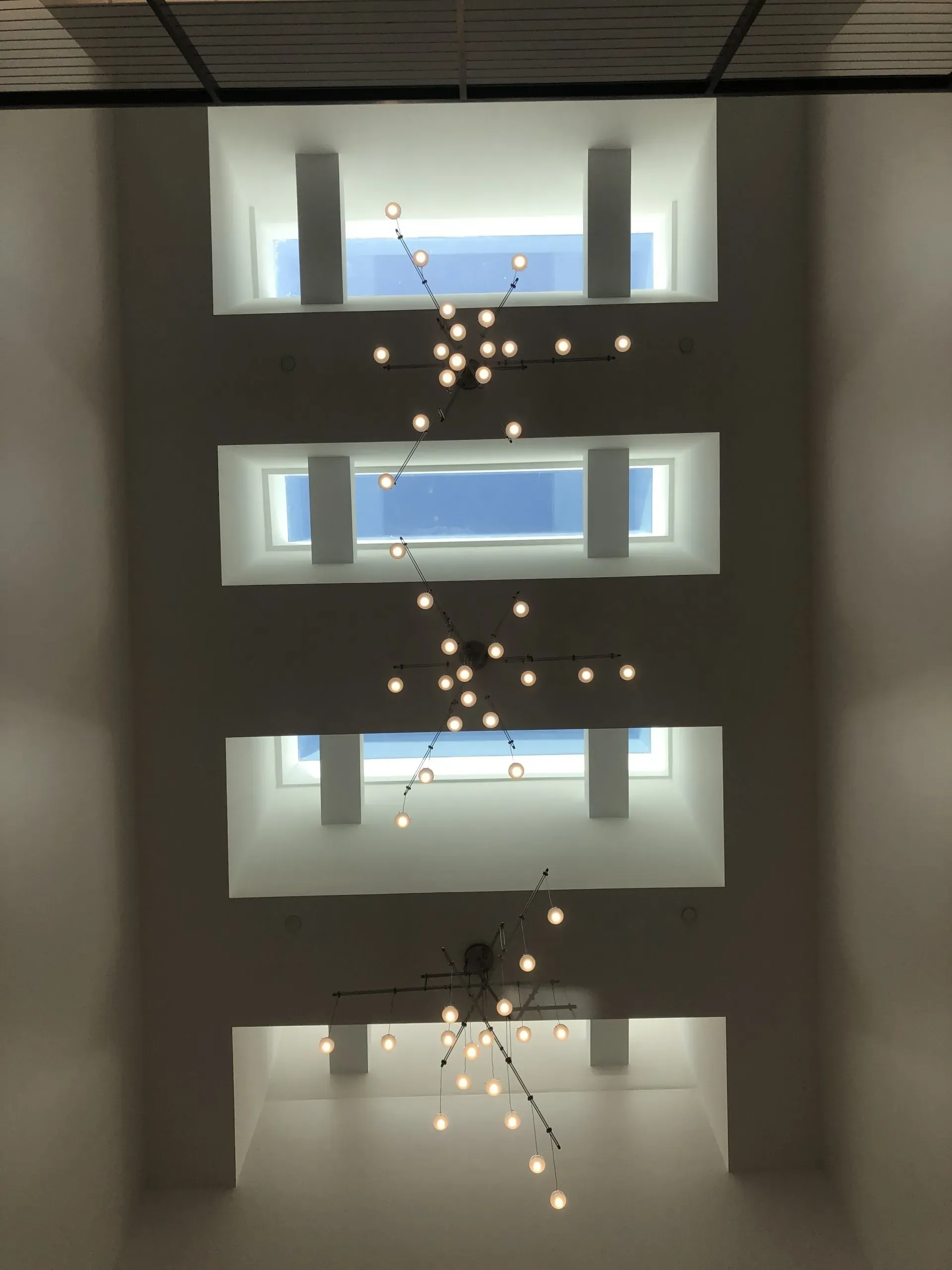 Interior atrium with stacked skylights and a hanging starburst chandelier against white walls