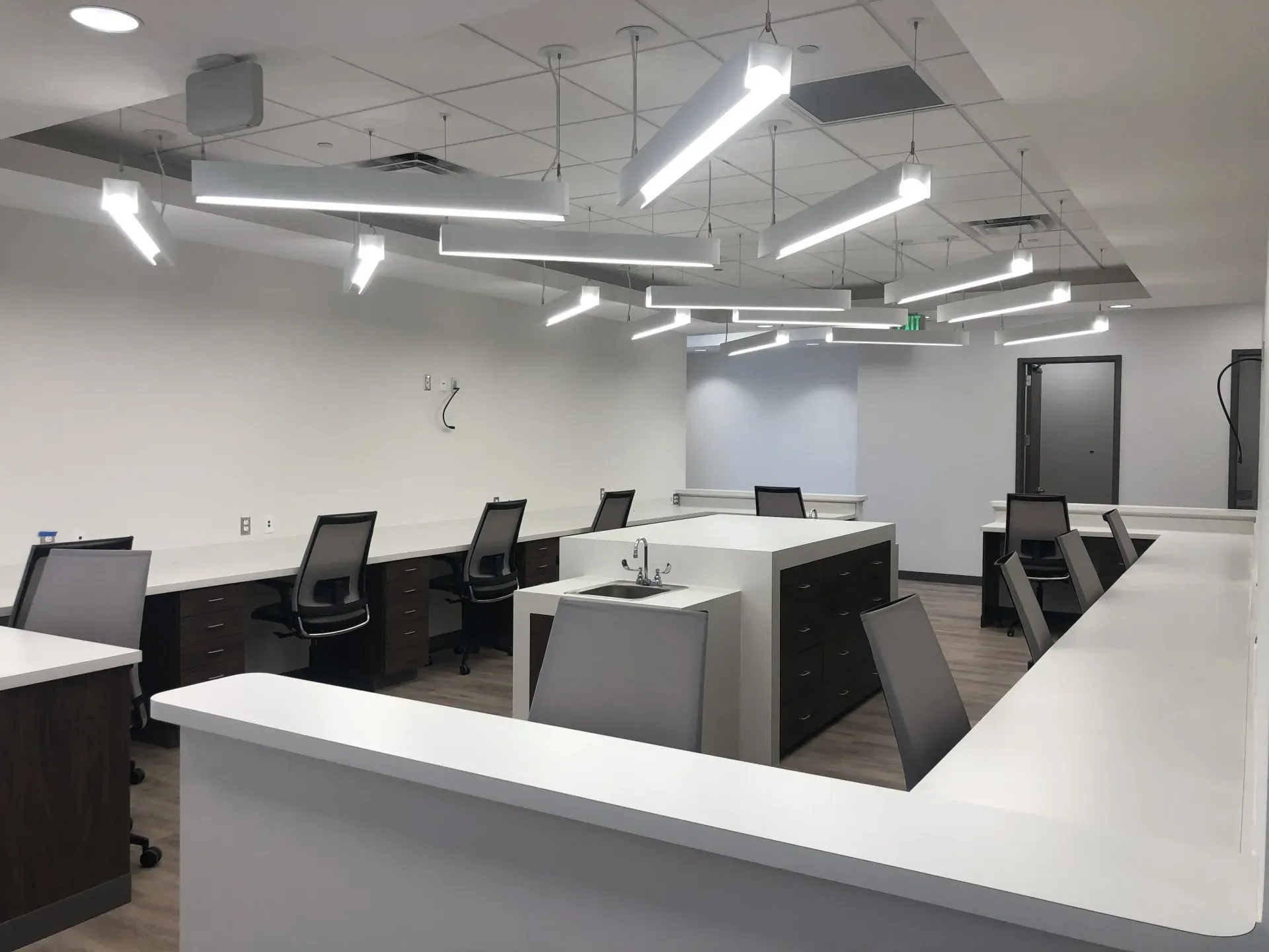 Modern office workspace with white desks, black chairs, and bright overhead lights in an open room