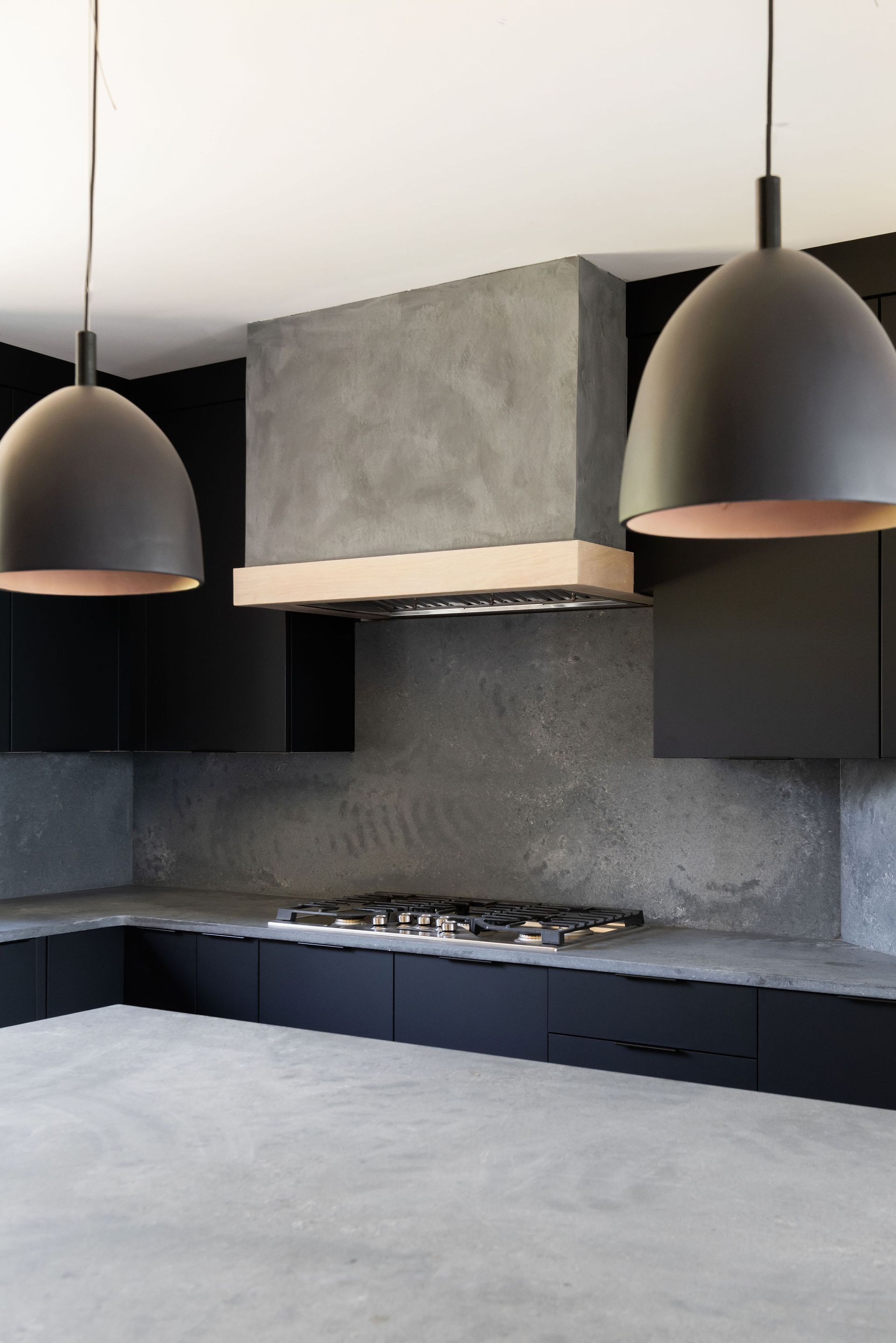Modern black-and-gray kitchen with pendant lights, stone backsplash, and built-in cooktop under a vent hood