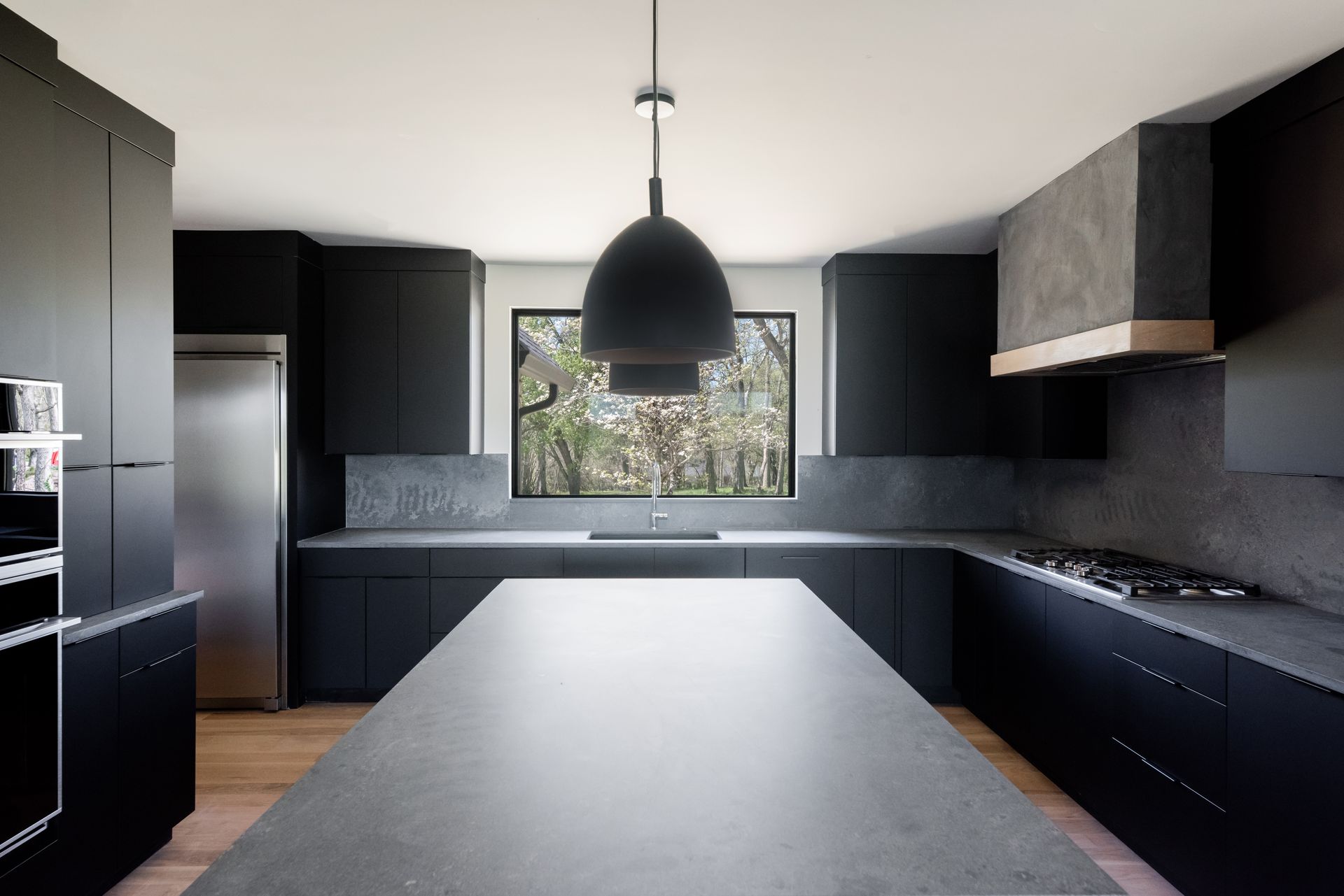 Modern black kitchen with central island, pendant light, and window above the sink