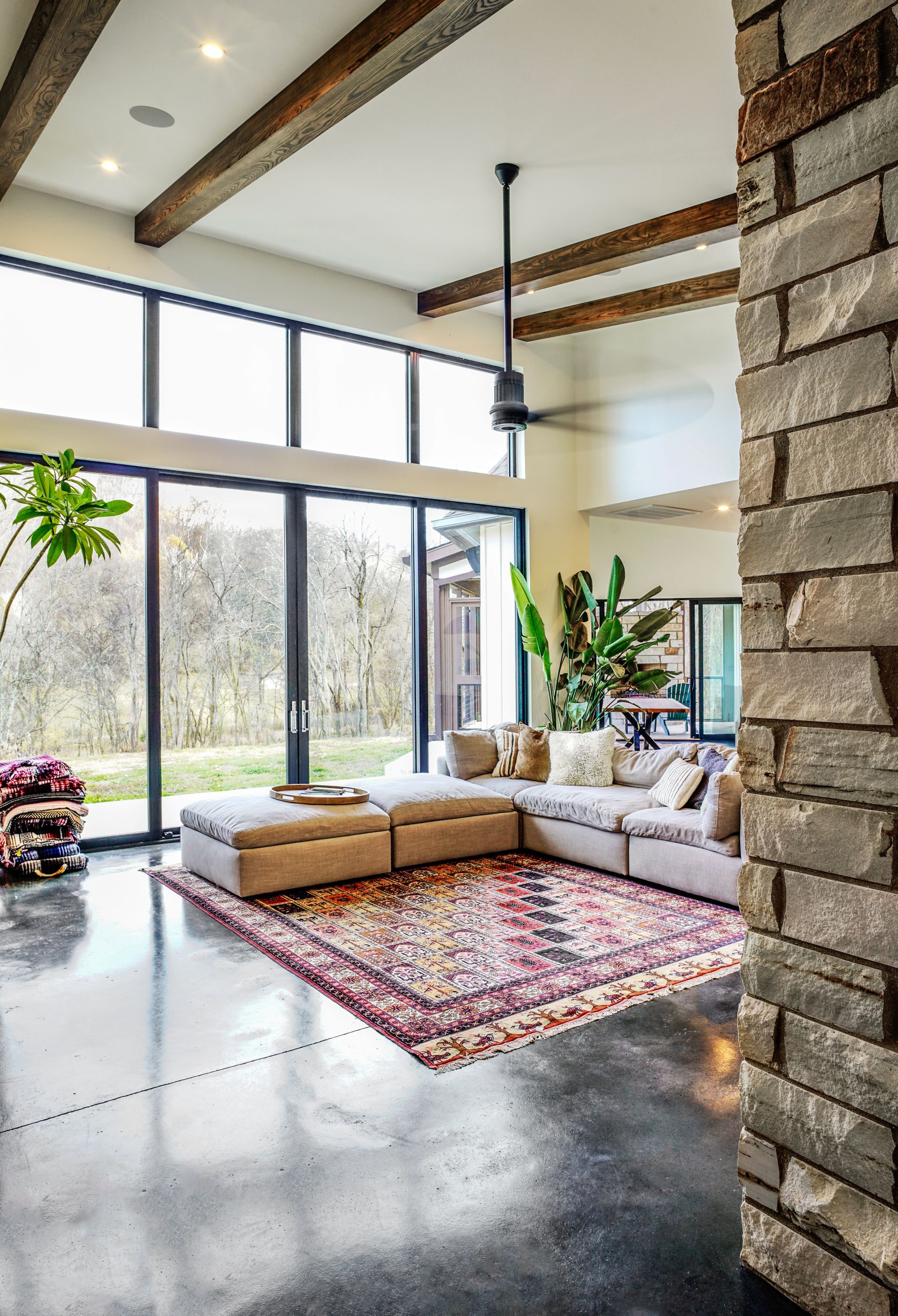 Bright modern living room with sectional sofa, patterned rug, large windows, and exposed wood beams