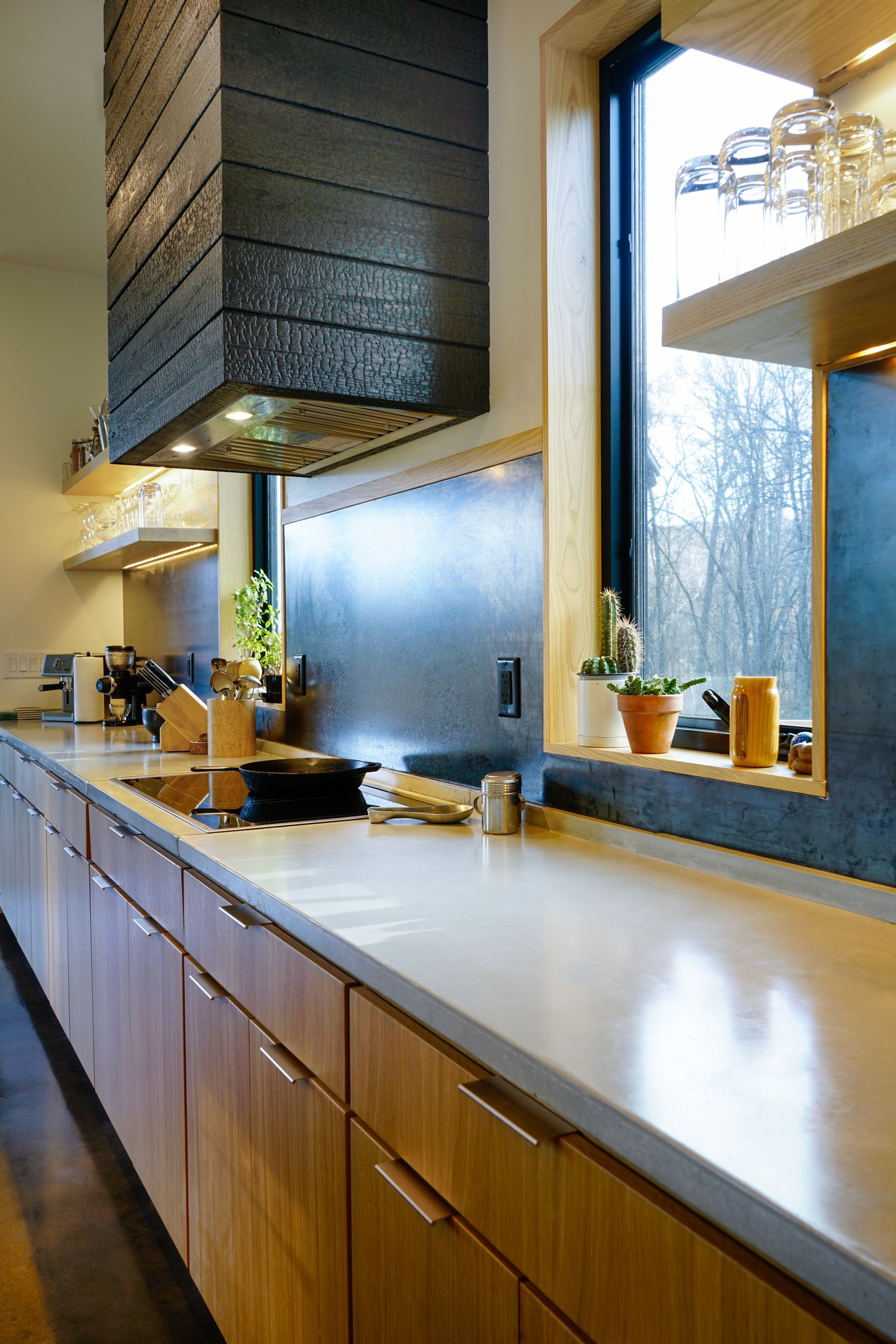 Modern kitchen with long white countertop, wood cabinets, frosted window, and hanging pots above the stove