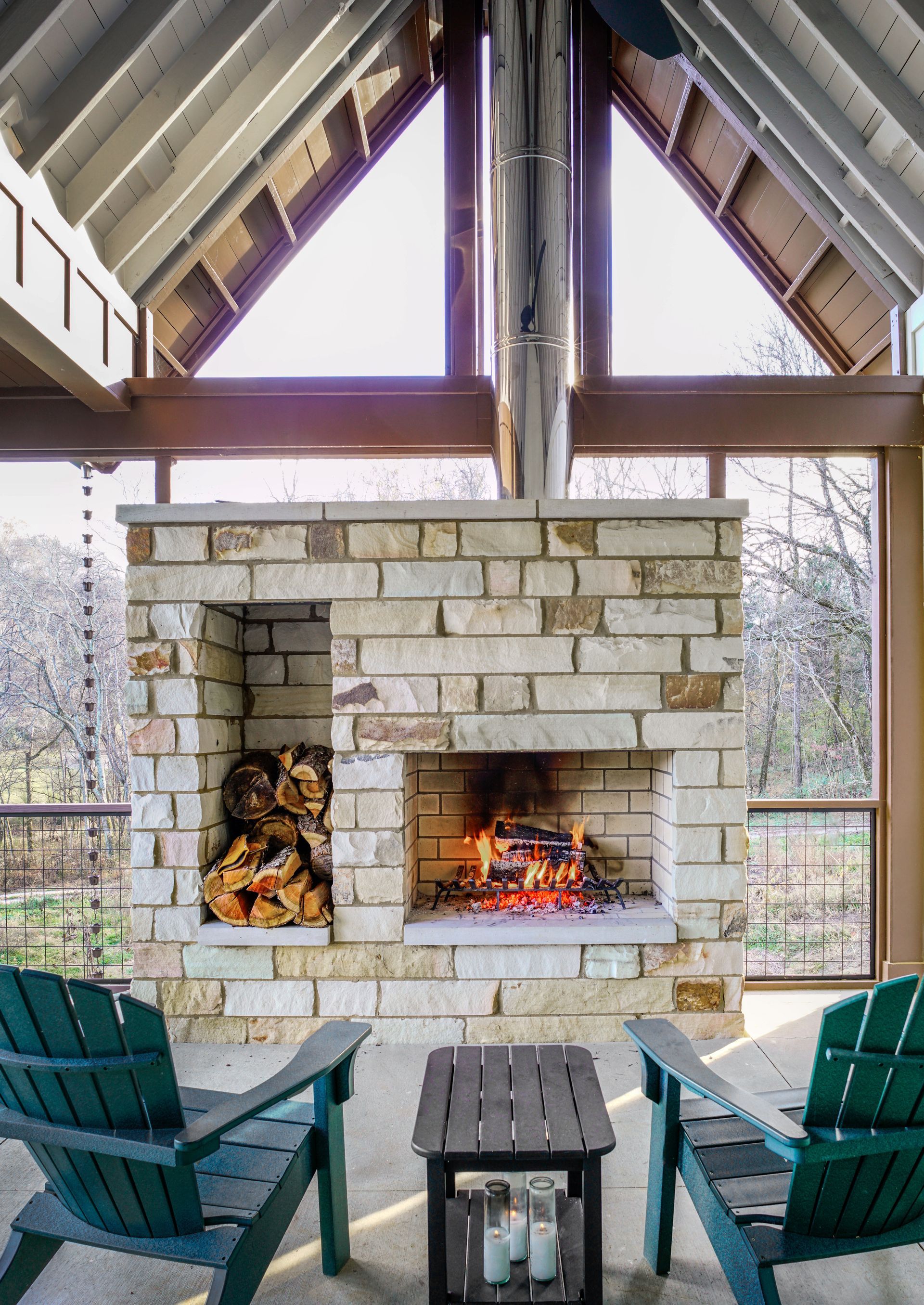 Covered patio with stone fireplace, burning fire, and teal chairs overlooking a yard