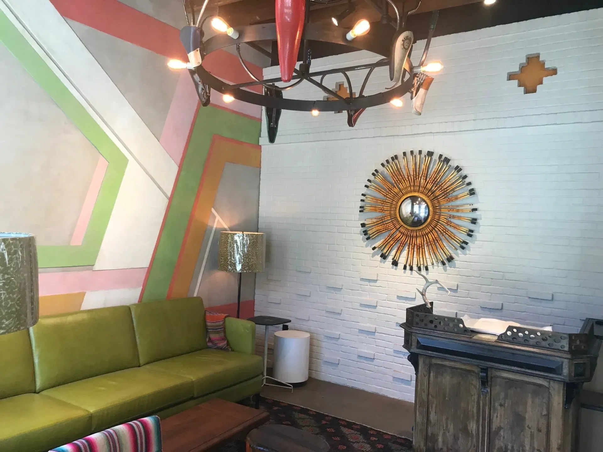 Colorful lounge with green sofa, patterned wall art, sunburst mirror, and rustic wooden table