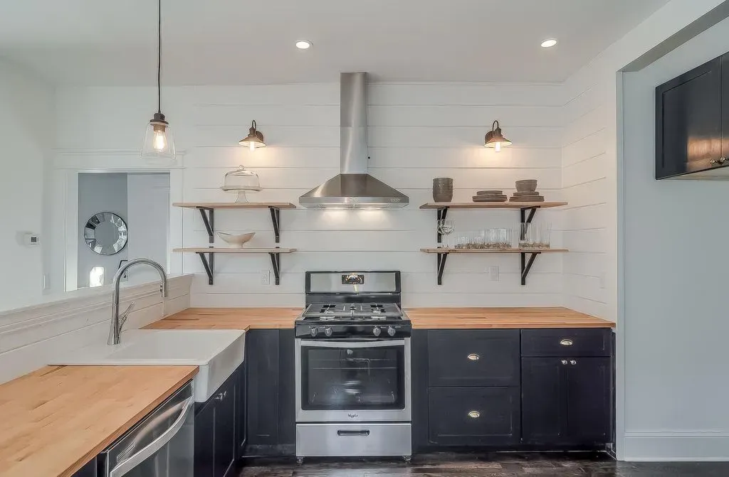 Modern white kitchen with wood countertops, black stove, open shelves, and stainless steel range hood