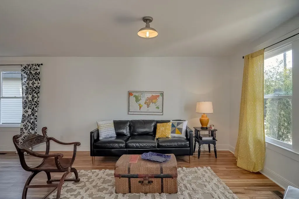 Bright living room with black sofa, wooden chair, world map art, yellow curtains, and large windows.