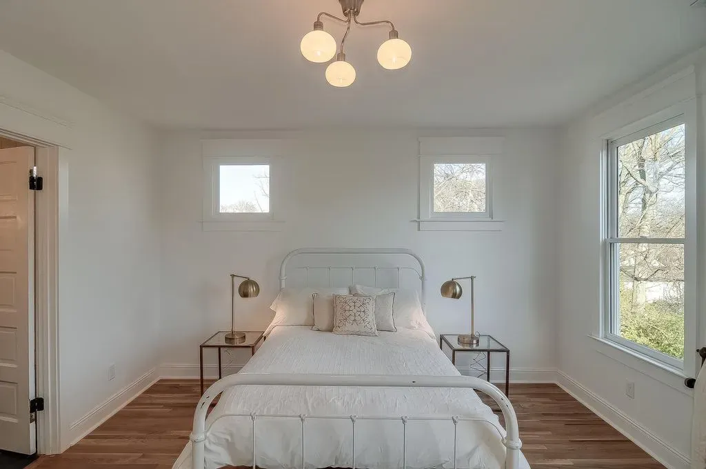 Bright, minimalist bedroom with white bedding, two windows, and a ceiling light fixture