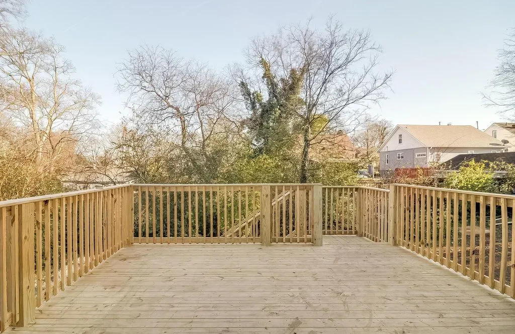 Wooden deck with railings overlooking bare trees and nearby houses under a clear sky