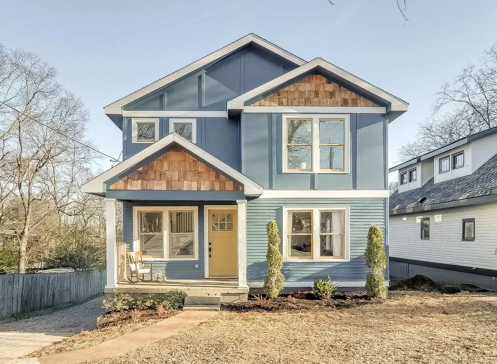 Blue two-story house with tan trim and a front porch in a sunny suburban yard