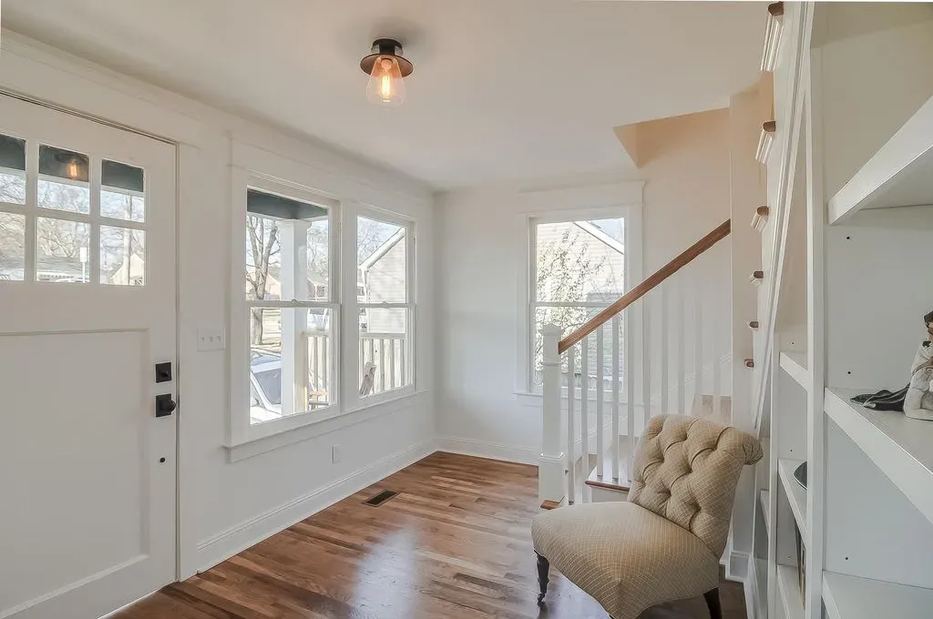 Bright entryway with white walls, wood floors, windows, staircase, and a tufted bench