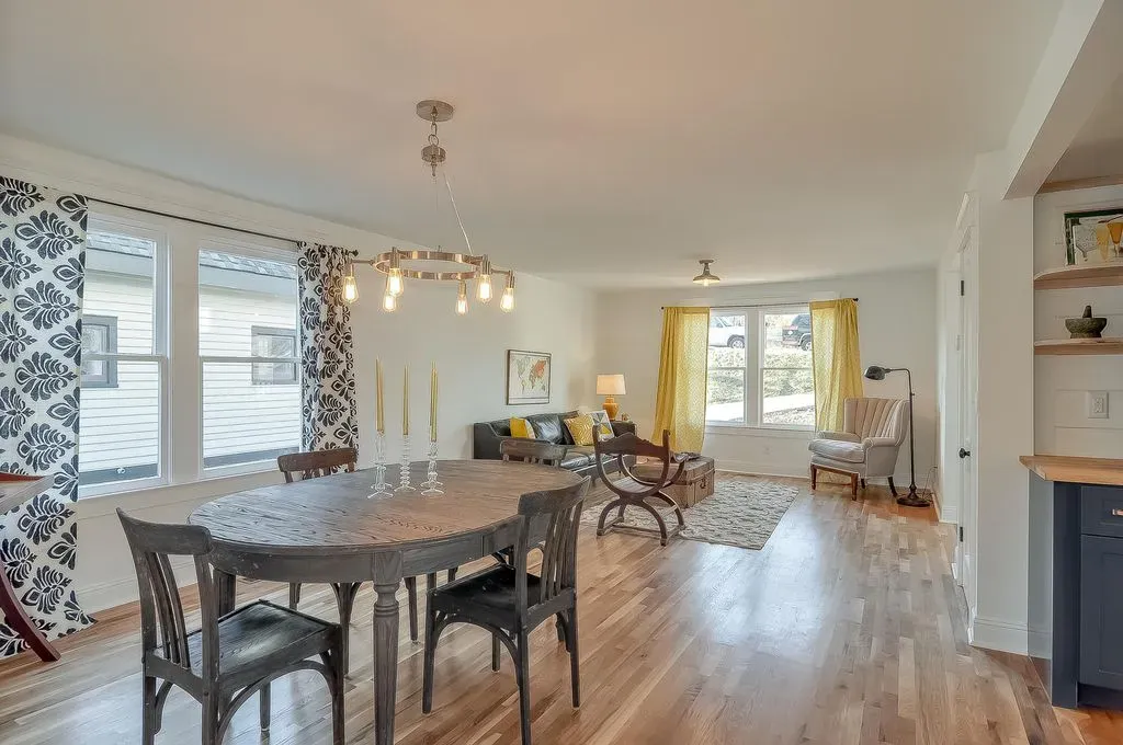 Bright dining and living room with hardwood floors, chandelier, patterned curtains, and large windows