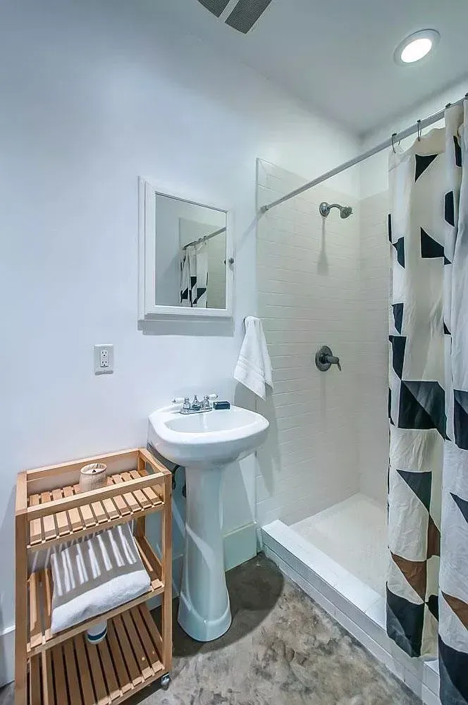 Small bathroom with pedestal sink, mirror, shower stall, and striped curtain.