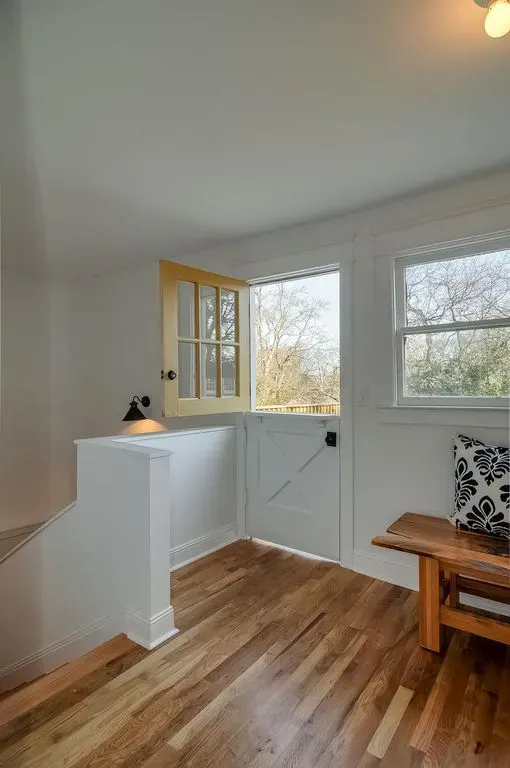 Bright white entryway with wood floors, a half door, windows, and a wooden bench with patterned pillow.