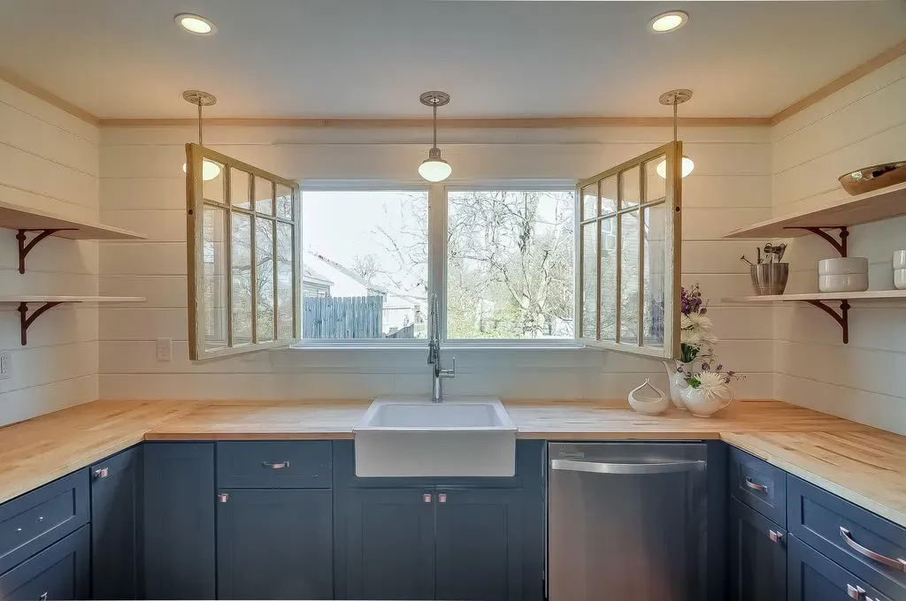 Modern kitchen with blue cabinets, wooden counters, farmhouse sink, and large window above the sink