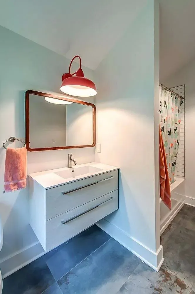 Modern bathroom vanity with white sink, red light fixture, and dark tile floor