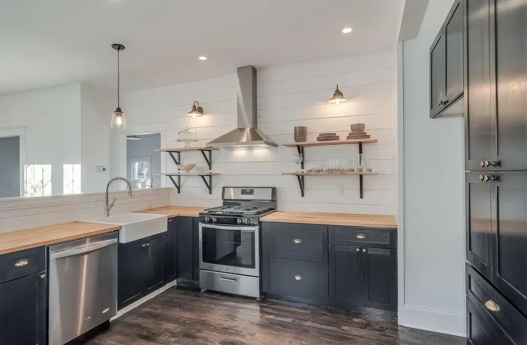 Modern kitchen with dark cabinets, white countertops, stainless appliances, and open wood shelves
