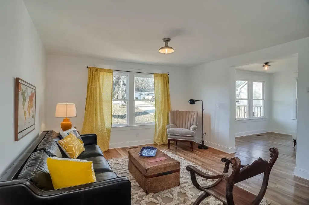Bright living room with black sofa, yellow accents, coffee table, armchair, and large windows with yellow curtains