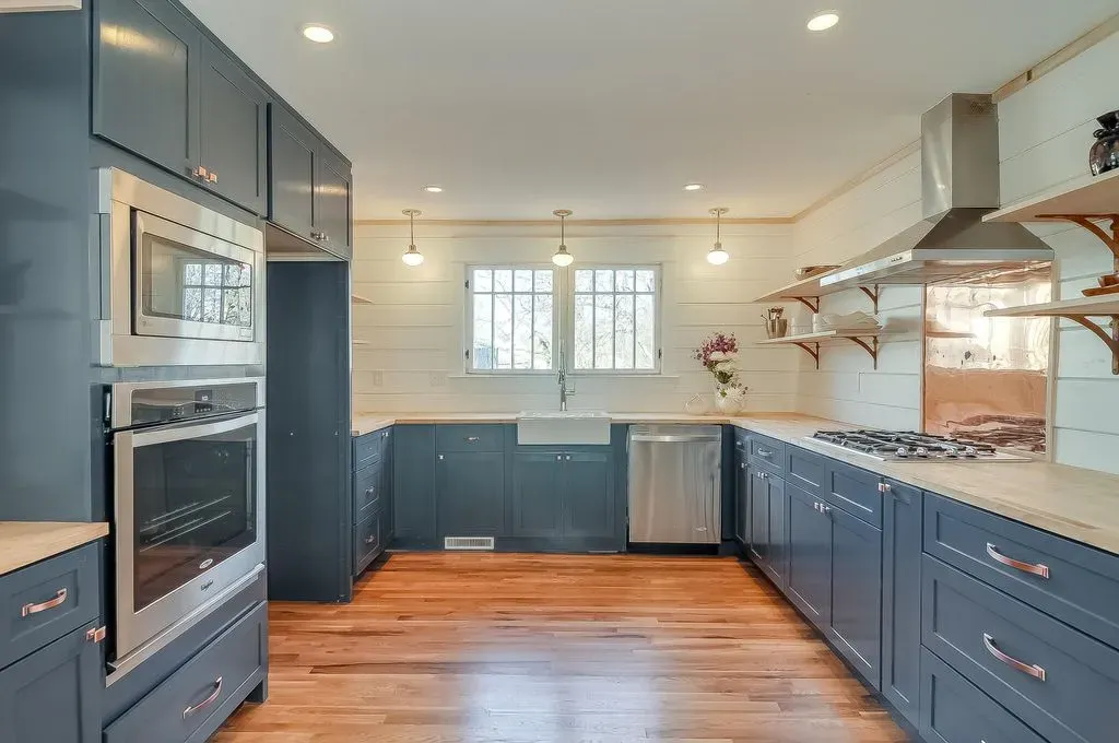 Bright modern kitchen with blue cabinets, stainless appliances, wood floors, and a window over the sink