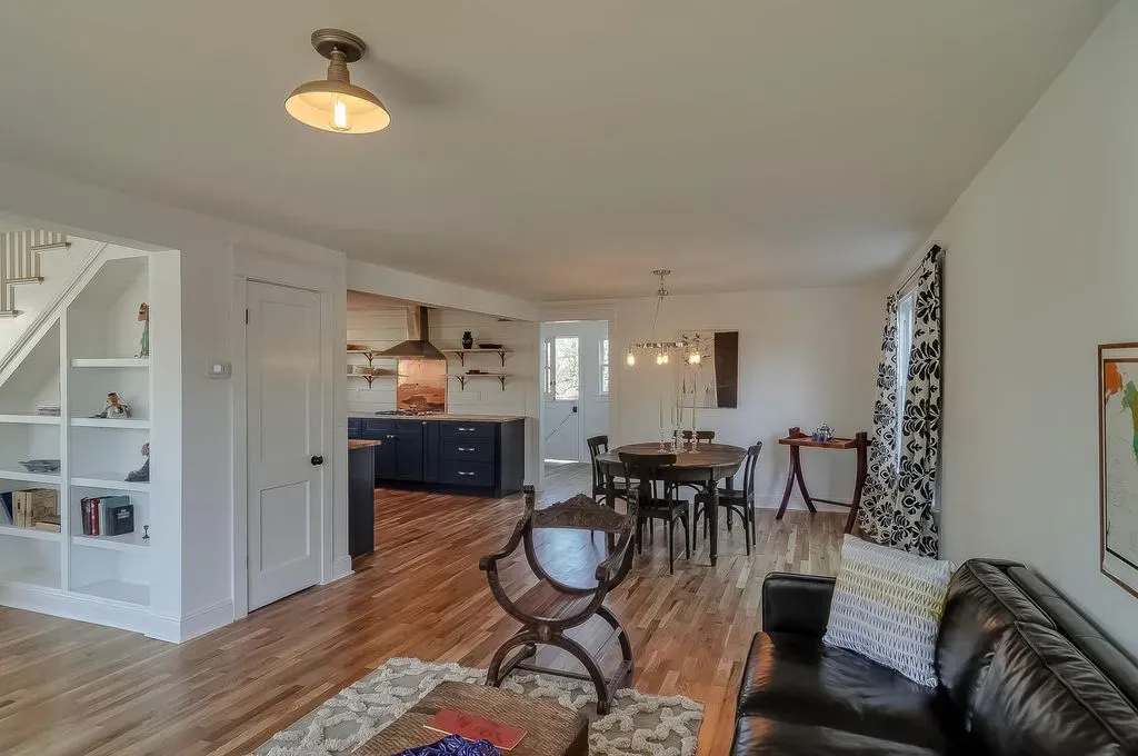 Open living room with hardwood floors, dark sofa, dining table, and kitchen visible in back.