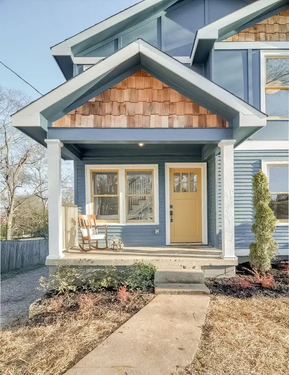 Blue house exterior with front porch, tan door, and landscaped yard under a gabled roof